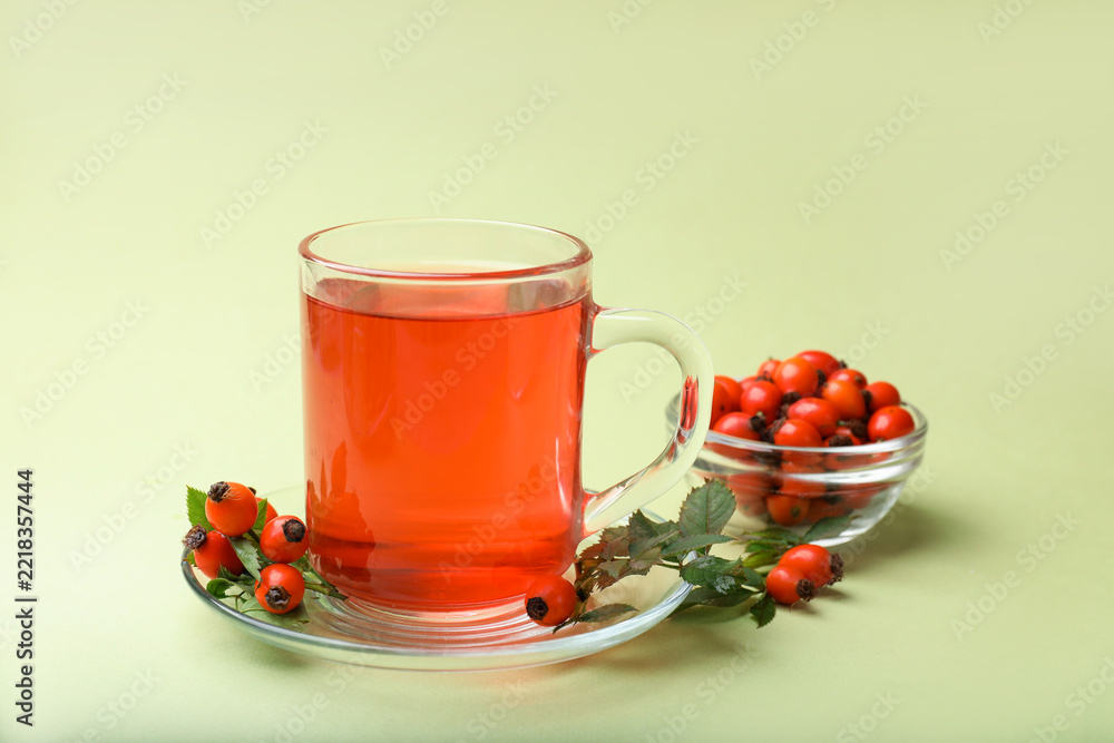 Fototapeta premium Rosehip tea in cup and berries with leaves on light green background