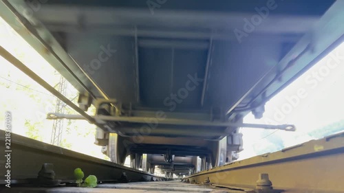 Camera placed on railway sleepers, dramatic low-angle view of train wagons rushing past at speed, industrial transport scene highlighting motion, fragility, and infrastructure power