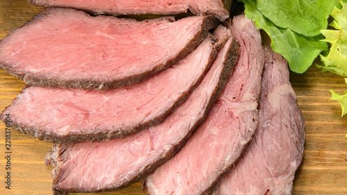 Sliced roasted beef arranged on wooden board with medium rare doneness and fresh herb garnish