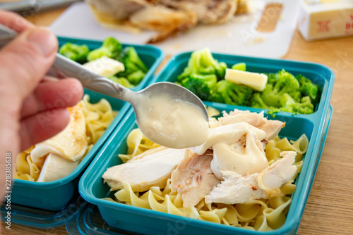 Meal Prep Easy Chicken Alfredo: hand using a spoon to drizzle creamy alfredo sauce over sliced chicken and noodles.