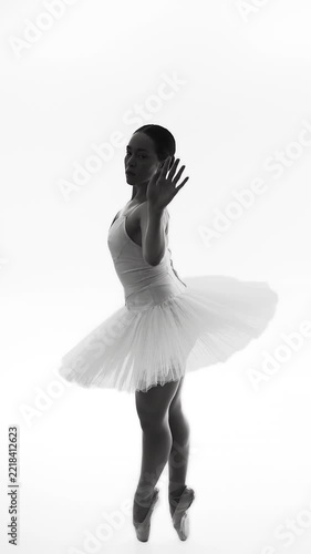 Professional ballet dancer performs graceful movement in white studio with dramatic lighting