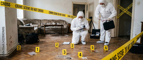 Forensic investigators in hazmat suits examine evidence at a crime scene marked with yellow tape and numbered markers