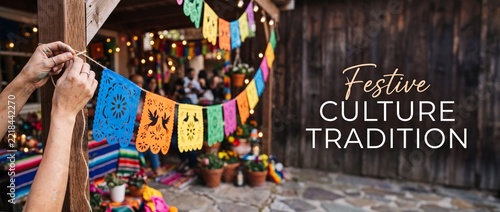 Mexican fiesta papel picado decorations being hung up by hands for outdoor party celebration, colorful traditional cut paper banner bunting, Cinco de Mayo, Dia de los Muertos event rustic background.