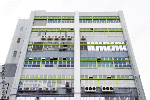 Modern commercial building facade viewed from low angle. Featuring rows of glass windows arranged in symmetrical geometric pattern and multiple air conditioning units installed along exterior walls.