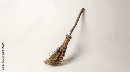 Rustic vintage wooden broom leaning against a plain light gray background