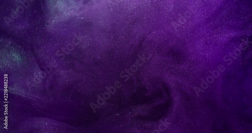 Ink splash. Mist art. Defocused purple lilac color sparkling liquid neon glitter texture spreading on abstract dark black art background.