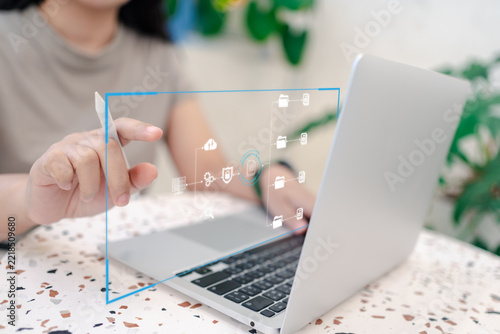 Close up of hand holding stylus pointing at glowing digital folder network interface over a laptop