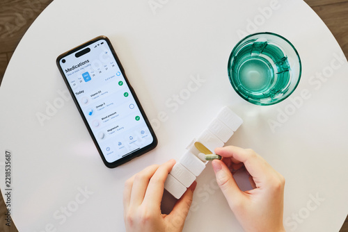 Female hands preparing daily pills from an organizer with medication tracking app on phone