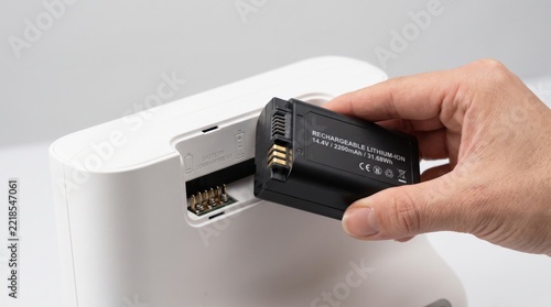 A hand inserts a rechargeable lithium-ion battery into a white electronic device, demonstrating battery replacement or installation.