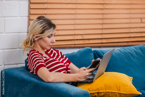 Woman shopping online with smartphone and laptop on sofa at home