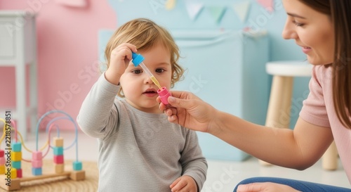 Mother and Toddler playing with medicine dropper in a colorful nursery. Learning through play.