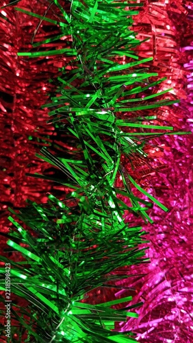 Colorful Christmas tinsel with green, pink and red metallic strands creating a vibrant vertical festive background for holiday designs.