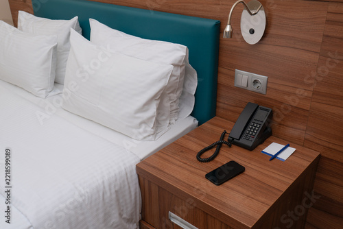 Modern hotel bedroom interior with comfortable bed, nightstand, and phone