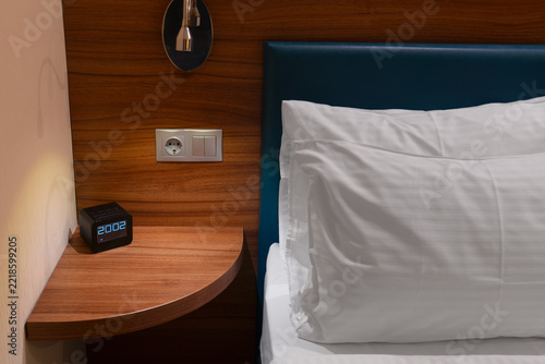 Modern hotel bedside with pillow, wooden shelf and digital clock