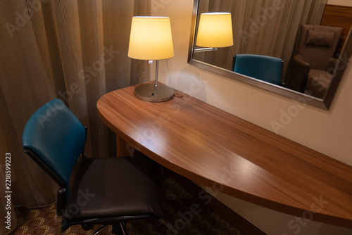 Modern hotel workspace with wooden desk, lamp and teal chair