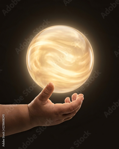 The child's hand holds back a glowing sphere with a mystical aura on a dark background, copy space