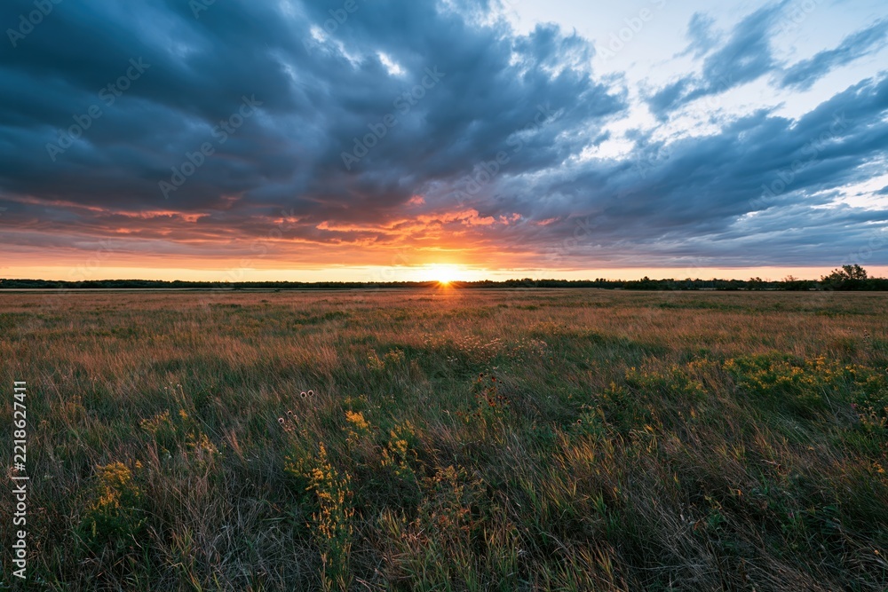 Naklejka premium The Sunset Over Open Prairie Field At Dusk With Dramatic Clouds