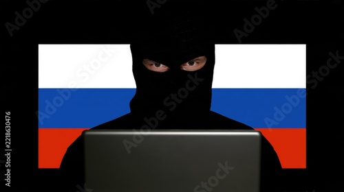 Russian hacker in balaclava at laptop is committing cybercrime. Espionage. Election meddling. State sponsored cyber attack, warfare, security breach