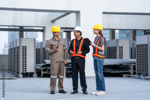 Technician engineer worker hard hat safety vest air conditioner inspection rooftop maintenance team discussing cooling equipment during commercial workplace safety check