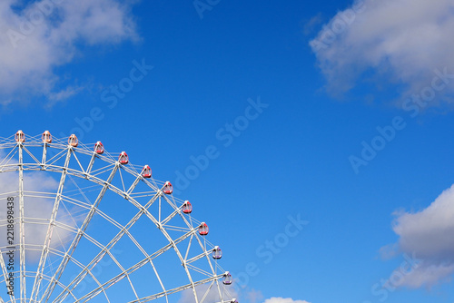 Part of large ferris wheel with red cabins against blue sky.