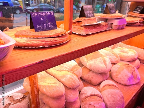 Obraz na plátně View of a traditional bakery display case showing a variety of rustic breads, loaves, baguettes, and freshly baked homemade empanadas with small descriptive chalkboard signs