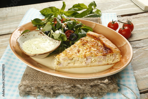 Slice of quiche with ham and salad on rustic plate