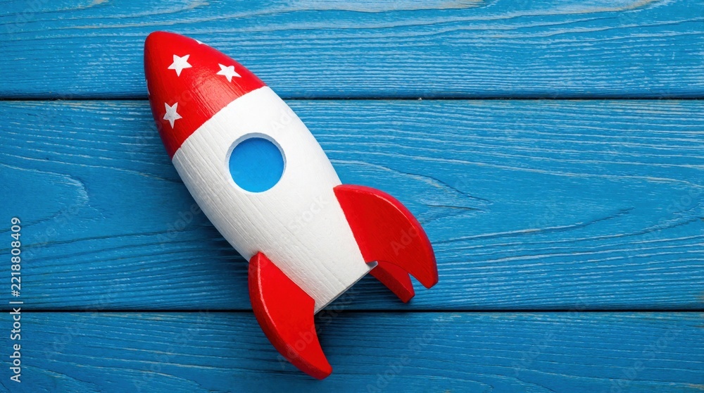 Fototapeta premium Colorful wooden toy rocket on blue wood background. Red, white spaceship model with star decor for kids. Creative childhood play concept about space travel, adventure, cosmic exploration. Fun object