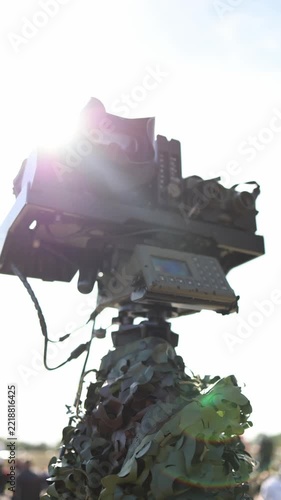 Vertical screen Military surveillance equipment with optical sensors and electronic controls mounted on a camouflaged observation station against bright sunlight and clear blue sky