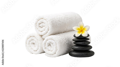 Soft white rolled towels stacked with a small pyramid of black wet massage stones and a single yellow plumeria flower, spa relaxation, wellness, serene atmosphere