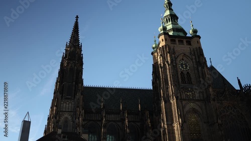 Saint Vitus Cathedral at Prague Castle rises with majestic Gothic spires a historic clock tower and an ornate medieval roof showcasing remarkable architecture against a clear blue sky