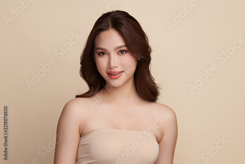 A beautiful young Asian woman with clean, fresh skin against a beige background. Skincare, facial treatment, cosmetology, beauty, and spa. An elegant portrait of an Asian woman.