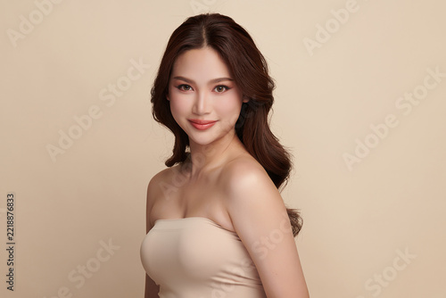 A beautiful young Asian woman with clean, fresh skin against a beige background. Skincare, facial treatment, cosmetology, beauty, and spa. An elegant portrait of an Asian woman.