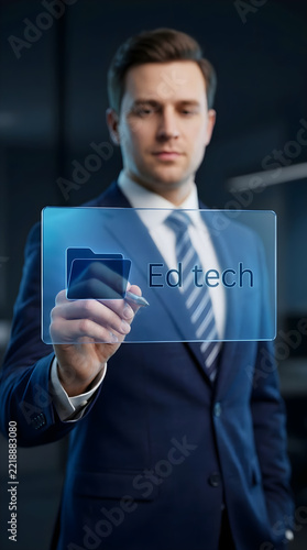 ​Businessman in formal suit interacting with futuristic digital transparent screen displaying Ed Tech folder icon and text in modern office