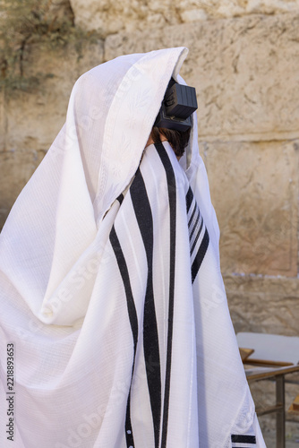 Man wrapped in a striped tallit with tefillin praying at the Western Wall in Jerusalem.