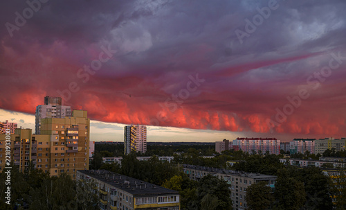 A crimson-purple sunset and a dark cloud over the houses in a city block.