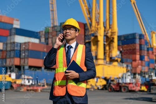 Asian american male customs broker talking on smart phone while looking at containers