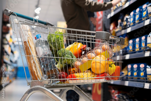 Full Shopping Cart with Groceries in Supermarket Aisle
 Copiar título