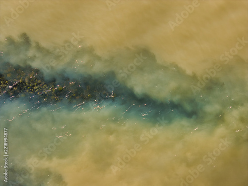 Aerial view of swirling sediment plumes in glacial river water, showing contrasting shades of turquoise and murky brown silt in Mulathing, Iceland.