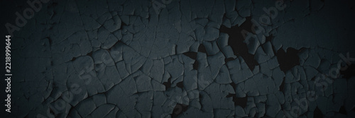 Dark wide panoramic background. Peeling paint on a concrete wall. Dark grunge texture of old cracked flaking paint. Weathered rough painted surface. Patterns of cracks. Darkness background for design.