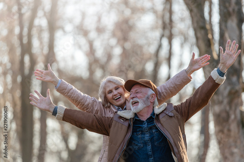 Cheerful senior man and woman enjoying playful movement together in a sunny park, representing active aging, physical wellbeing and a joyful retirement lifestyle