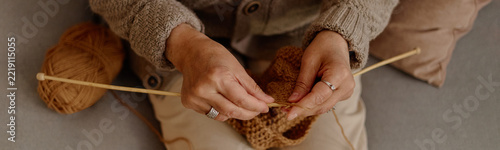 Senior woman knitting with wooden needles and yarn ball at community hobby club. Suitable for retirement leisure marketing, elderly craft workshop promotion, close up