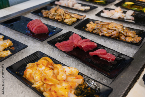 Assorted fresh seafood including tuna and shellfish arranged on black plates over crushed ice at a restaurant buffet. Raw food that visitors prepare themselves.