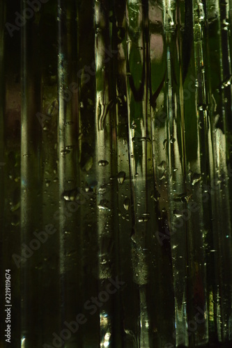 Abstract close up of dark green glass texture with vertical ridges and trapped air bubbles inside