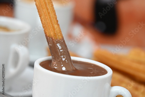 churros with hot chocolate and coffee, traditional golden churros served with a cup of thick hot chocolate and coffee on a cafe table, with a hand dipping a churro into chocolate