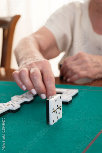 Senior hand playing dominoes game on green table