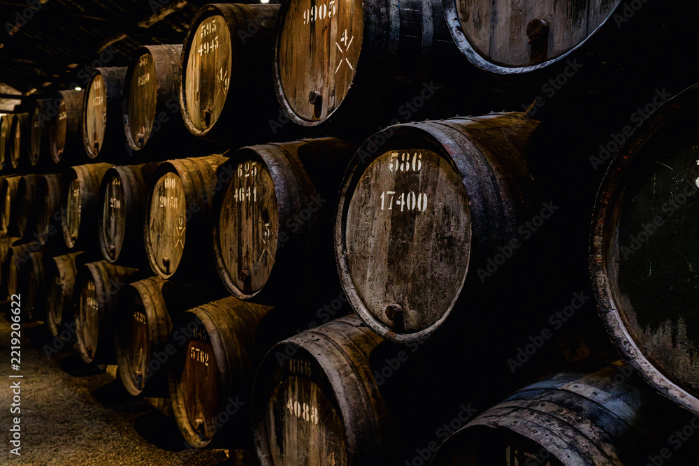 Fototapeta premium Interior of traditional wine cellar in Porto Portugal with rows of wooden barrels used for aging port wine. Atmospheric underground storage with perspective view and warm low lighting.