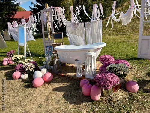 Rustic outdoor bathtub photoshoot setup with pink pumpkins and flowers
