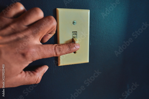 Hand Flipping a Toggle Light Switch on a Dark Blue Wall