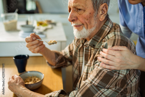 Caregiver comforting senior man eating oatmeal at home