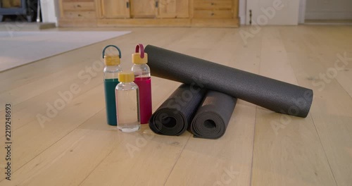 Camera is panning slightly, revealing wooden cabinet, pale rug, three black mats and water bottles